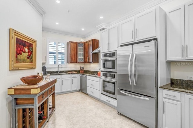 kitchen with stainless steel appliances, crown molding, sink, dark stone countertops, and white cabinets