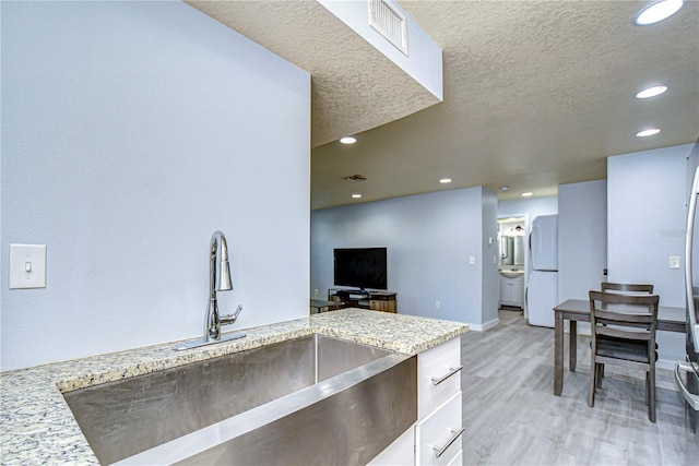 kitchen with light stone counters, light hardwood / wood-style floors, a textured ceiling, sink, and white fridge