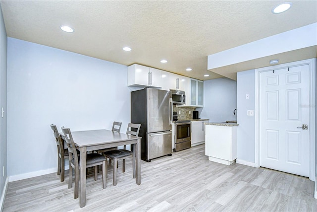 kitchen with light hardwood / wood-style flooring, a textured ceiling, decorative backsplash, white cabinets, and appliances with stainless steel finishes