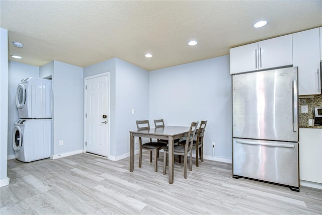 dining room with light hardwood / wood-style flooring, stacked washing maching and dryer, and a textured ceiling