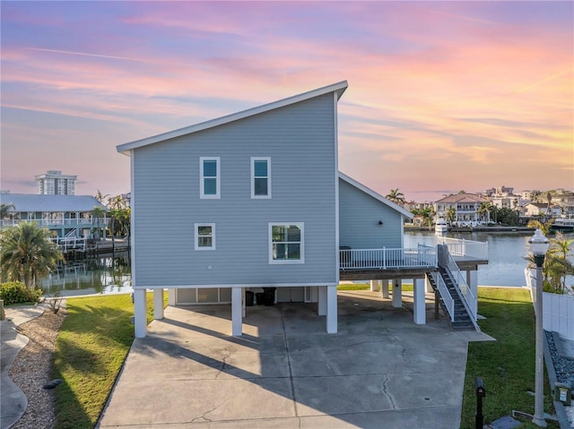 back house at dusk with a yard, a water view, and a carport