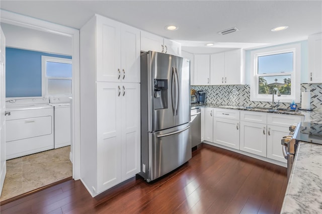 kitchen with decorative backsplash, appliances with stainless steel finishes, light stone countertops, washer and dryer, and white cabinetry