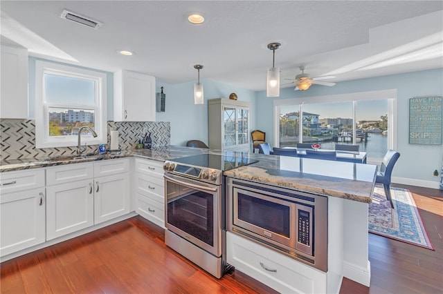 kitchen with kitchen peninsula, decorative backsplash, stainless steel appliances, and white cabinetry