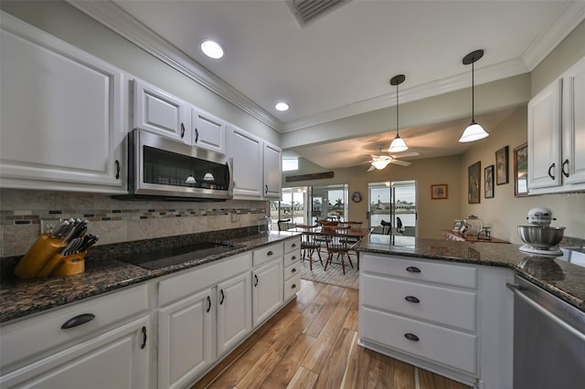 kitchen with appliances with stainless steel finishes, pendant lighting, white cabinets, ornamental molding, and light hardwood / wood-style flooring