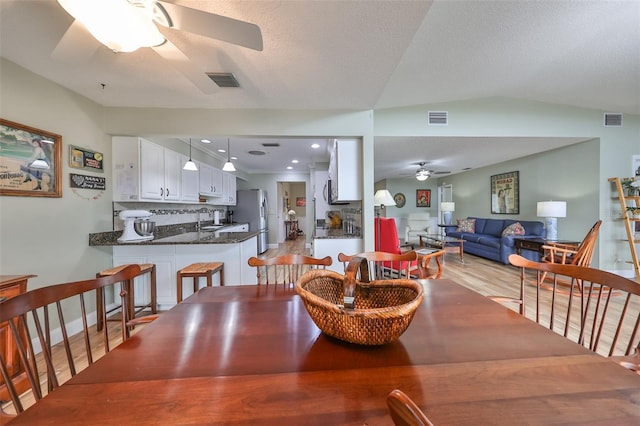 dining area with sink, a textured ceiling, ceiling fan, and light wood-type flooring