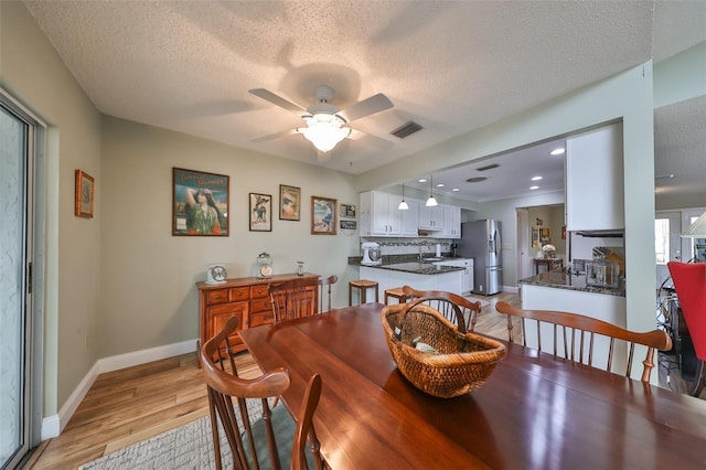 dining space featuring ceiling fan, light hardwood / wood-style flooring, sink, and a textured ceiling