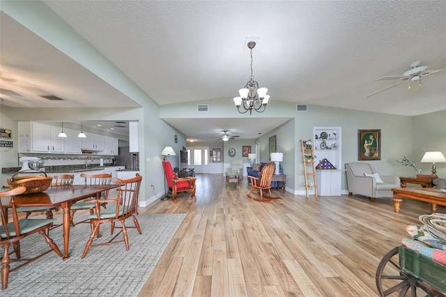 dining room featuring lofted ceiling, ceiling fan with notable chandelier, light hardwood / wood-style flooring, and a textured ceiling