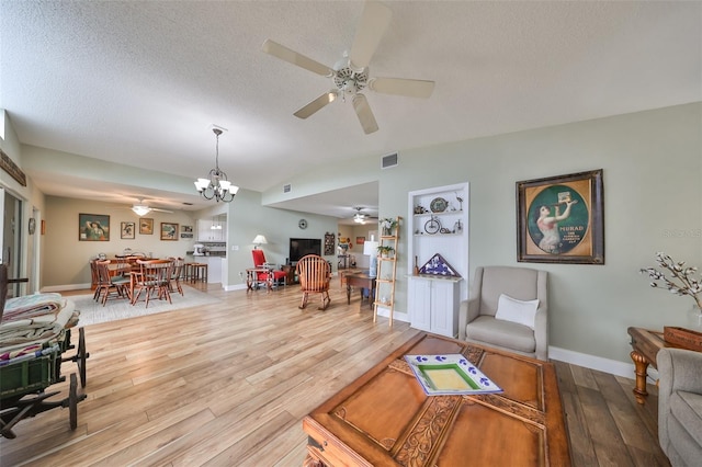 living room featuring hardwood / wood-style flooring, lofted ceiling, ceiling fan with notable chandelier, and a textured ceiling