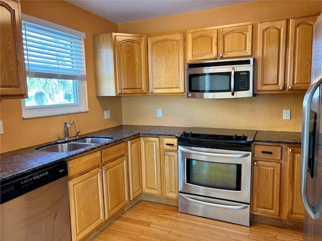 kitchen with dark stone countertops, sink, stainless steel appliances, and light hardwood / wood-style flooring