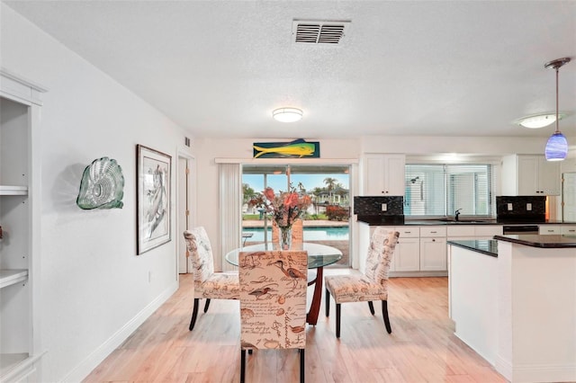 dining space with a textured ceiling, light wood-type flooring, and sink