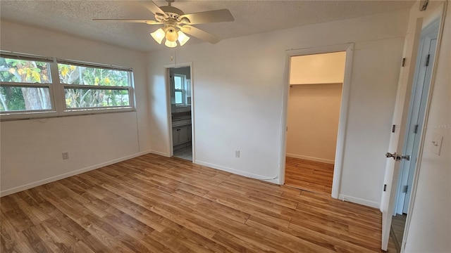 unfurnished bedroom featuring a walk in closet, light hardwood / wood-style flooring, ceiling fan, connected bathroom, and a closet