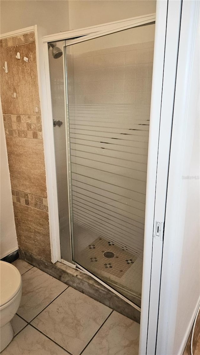 bathroom with tile patterned flooring, toilet, and a shower with shower door