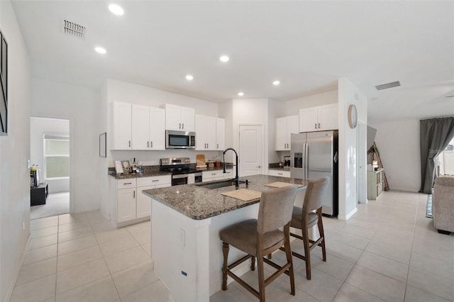 kitchen featuring a kitchen bar, dark stone counters, stainless steel appliances, sink, and an island with sink