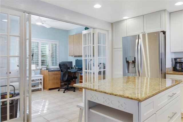 kitchen featuring stainless steel fridge, white cabinetry, ceiling fan, and light stone counters