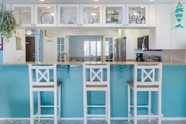 kitchen with a kitchen breakfast bar, stainless steel appliances, white cabinetry, and light stone counters