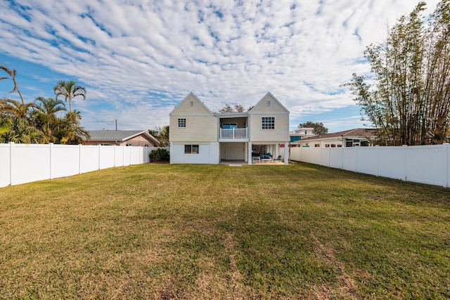 rear view of property featuring a balcony, a yard, and a patio