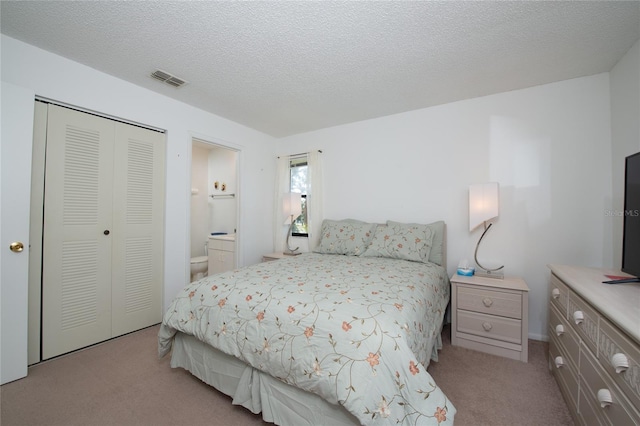 carpeted bedroom with a textured ceiling, ensuite bath, and a closet