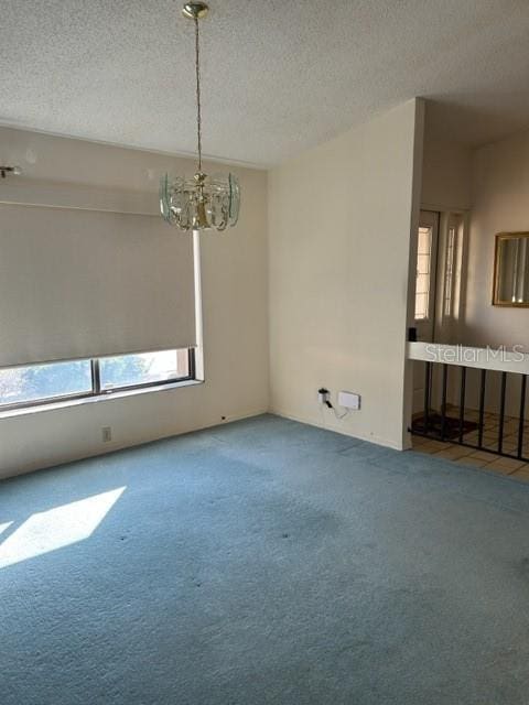 spare room with carpet flooring, a textured ceiling, and a notable chandelier