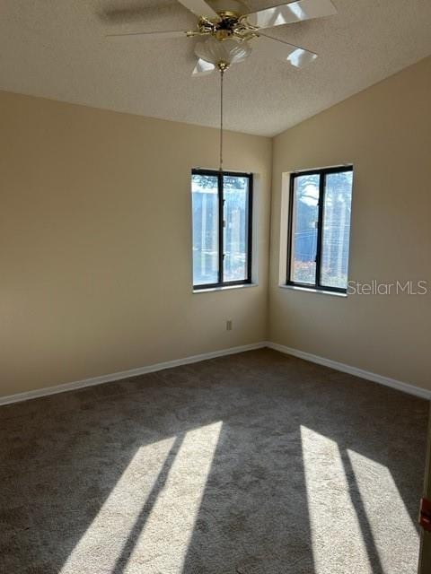 empty room featuring dark colored carpet, ceiling fan, a textured ceiling, and vaulted ceiling