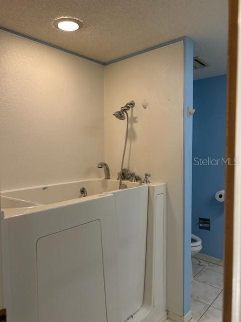 bathroom with a bathing tub, tile patterned flooring, a textured ceiling, and toilet