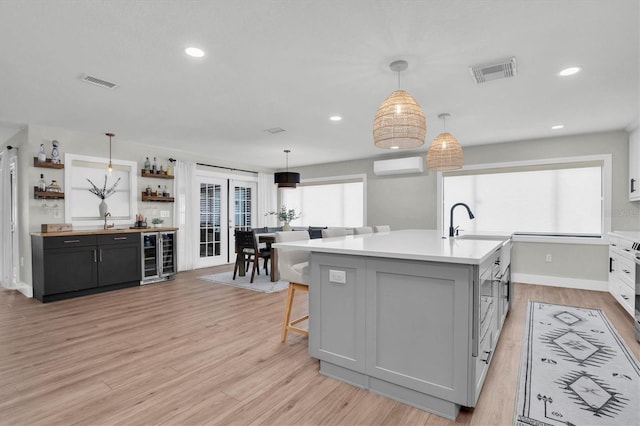 kitchen featuring hanging light fixtures, wine cooler, light hardwood / wood-style flooring, a wall mounted AC, and an island with sink