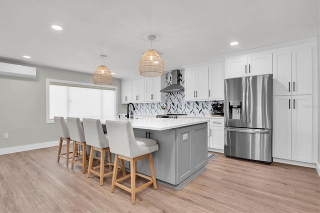 kitchen featuring white cabinets, stainless steel fridge, a wall mounted AC, and wall chimney exhaust hood