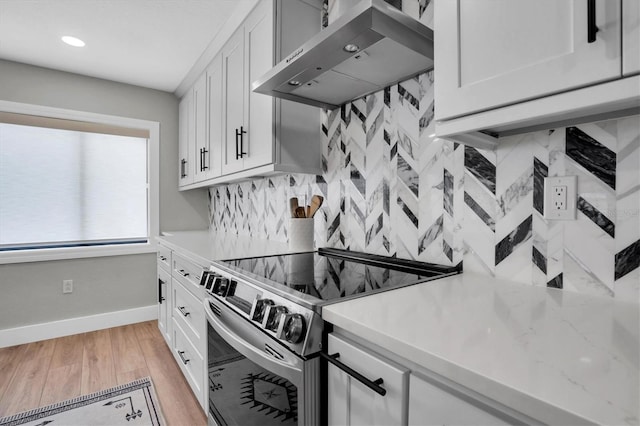 kitchen featuring tasteful backsplash, white cabinetry, stainless steel range with electric cooktop, and wall chimney range hood