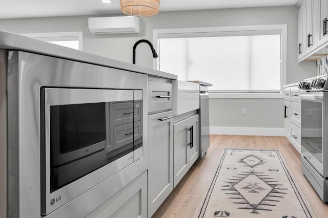 kitchen featuring stainless steel range, light wood-type flooring, white cabinetry, and a wall mounted AC