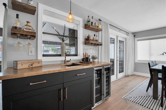 bar with wooden counters, light wood-type flooring, sink, wine cooler, and hanging light fixtures