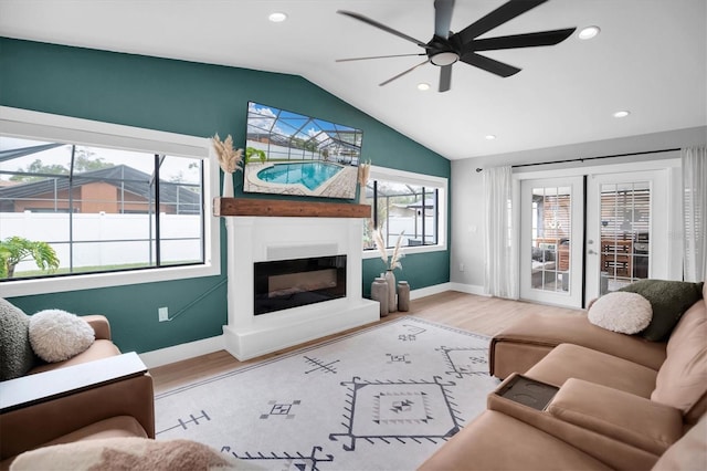 living room with ceiling fan, french doors, a large fireplace, light hardwood / wood-style floors, and vaulted ceiling