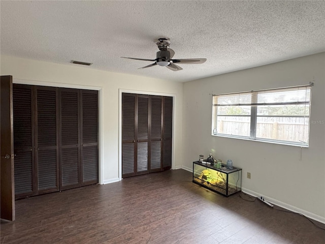 unfurnished bedroom featuring ceiling fan, a textured ceiling, and multiple closets