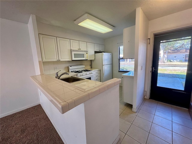 kitchen with white appliances, sink, kitchen peninsula, tile counters, and white cabinetry