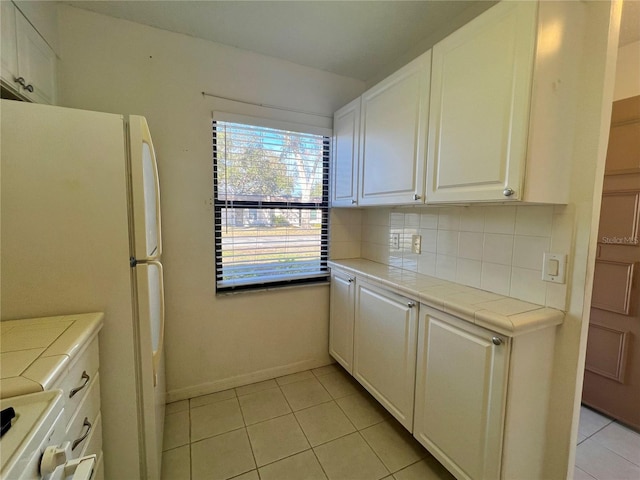 kitchen with tile counters, white refrigerator, white cabinetry, and light tile patterned floors