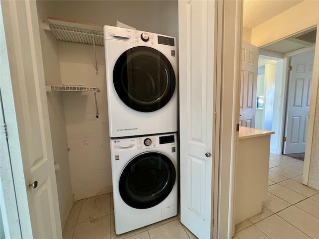 laundry area with light tile patterned flooring, stacked washing maching and dryer, and a textured ceiling