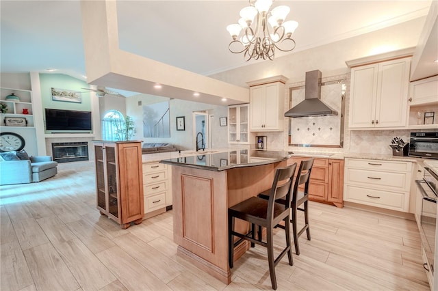 kitchen featuring wall chimney exhaust hood, a breakfast bar area, decorative light fixtures, a center island, and backsplash