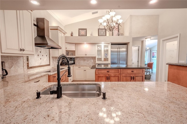 kitchen with stainless steel built in refrigerator, lofted ceiling, decorative backsplash, hanging light fixtures, and wall chimney range hood