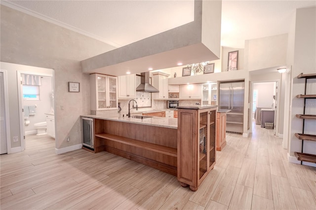 kitchen featuring sink, built in fridge, white cabinetry, kitchen peninsula, and wall chimney exhaust hood