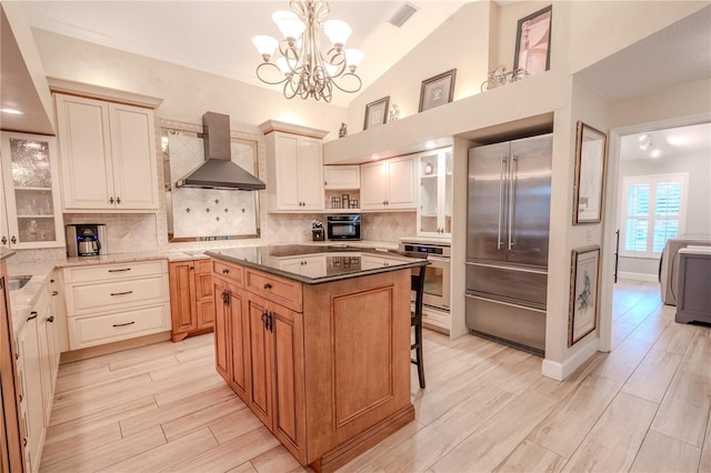 kitchen with vaulted ceiling, appliances with stainless steel finishes, pendant lighting, a center island, and wall chimney range hood