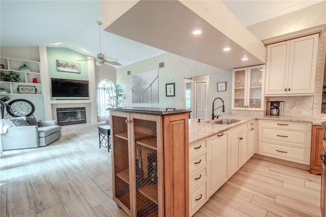 kitchen with light stone counters, lofted ceiling, kitchen peninsula, and sink