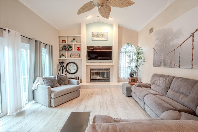 living room featuring lofted ceiling, crown molding, a tile fireplace, ceiling fan, and wood-type flooring