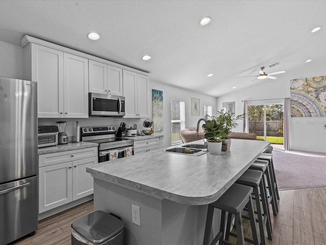 kitchen with lofted ceiling, a kitchen island with sink, white cabinets, appliances with stainless steel finishes, and a breakfast bar area