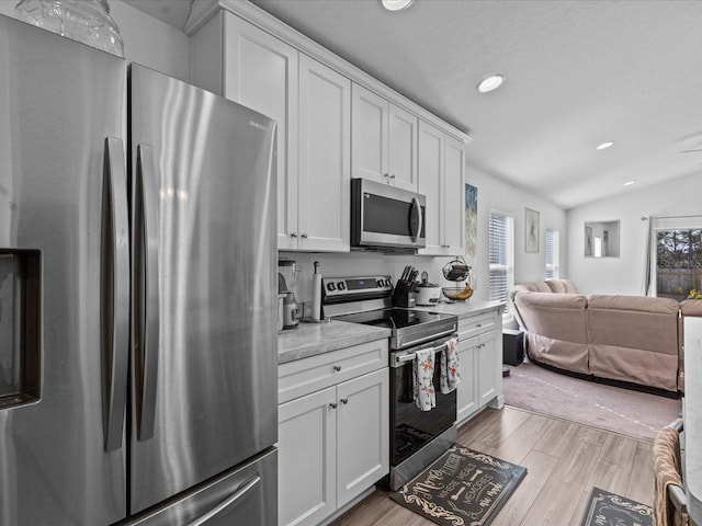 kitchen with a healthy amount of sunlight, white cabinets, stainless steel appliances, and vaulted ceiling