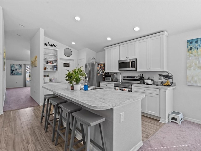 kitchen with a breakfast bar, lofted ceiling, a center island with sink, white cabinets, and appliances with stainless steel finishes