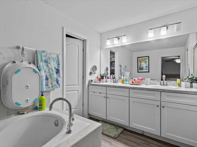 bathroom featuring wood-type flooring, vanity, and a relaxing tiled tub