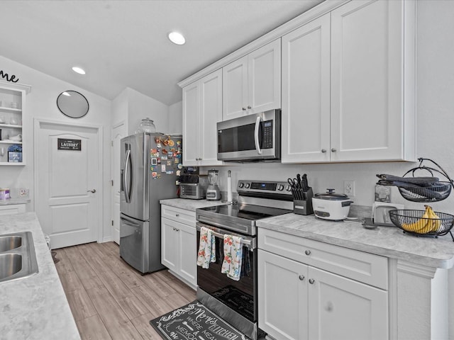 kitchen with sink, stainless steel appliances, lofted ceiling, white cabinets, and light wood-type flooring