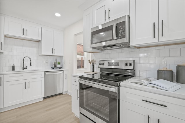 kitchen featuring sink, white cabinets, light wood-type flooring, backsplash, and appliances with stainless steel finishes