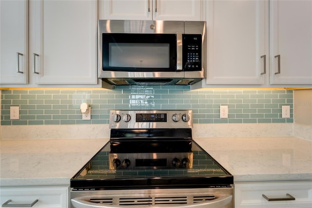 kitchen with white cabinets, appliances with stainless steel finishes, decorative backsplash, and light stone countertops