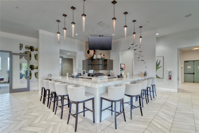 kitchen with light stone counters, kitchen peninsula, decorative light fixtures, a kitchen bar, and light parquet flooring