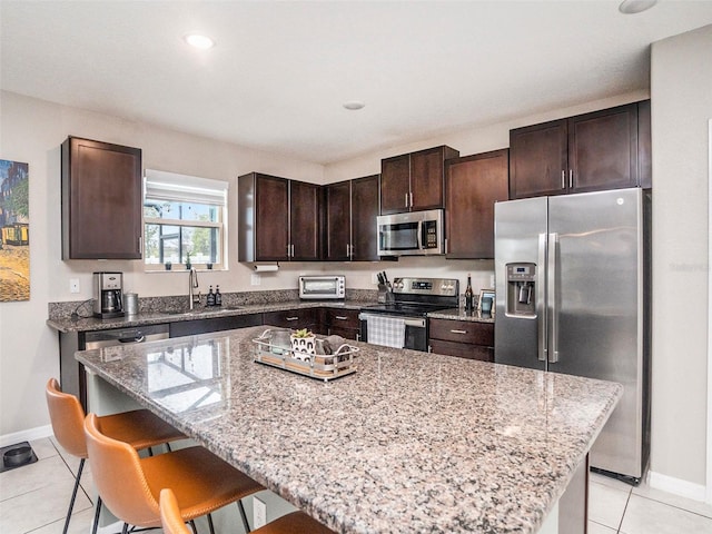 kitchen with stainless steel appliances, a center island, a kitchen bar, sink, and light tile patterned flooring