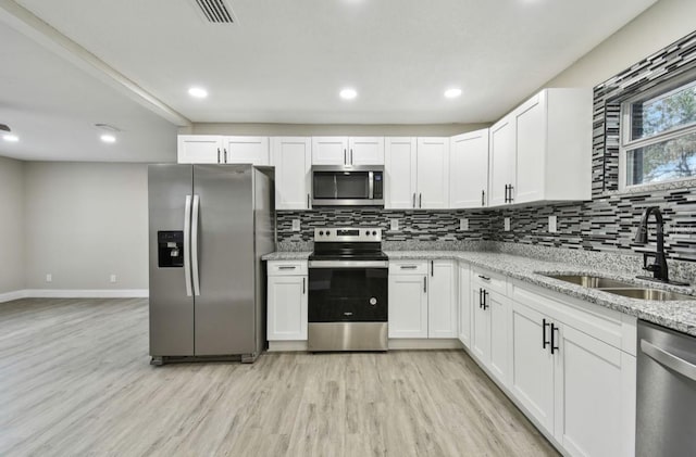 kitchen with light stone counters, stainless steel appliances, white cabinetry, and sink